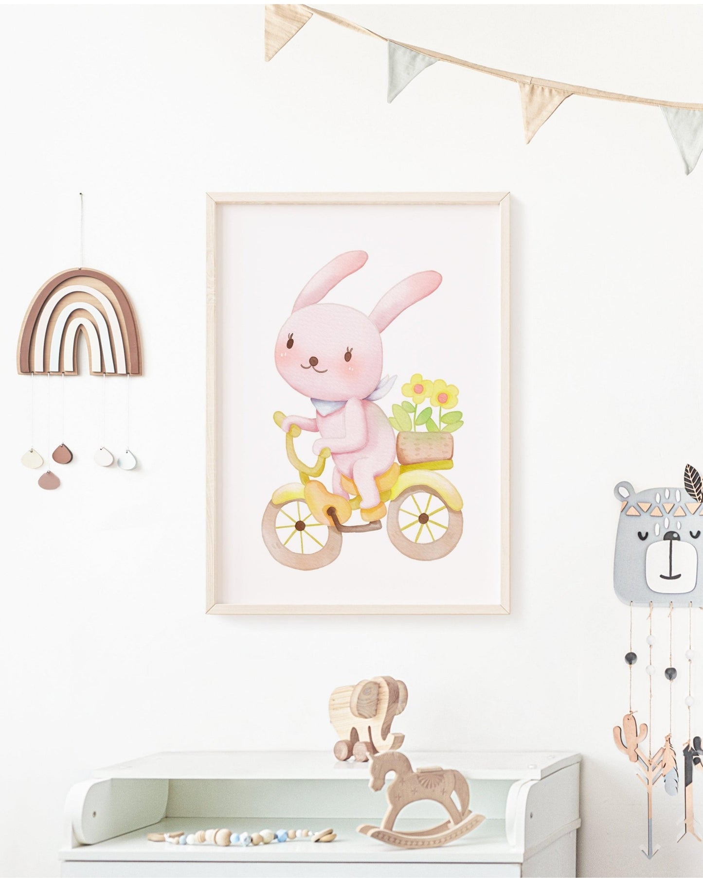 Poster con coniglietto rosa in bicicletta appeso alla parete di una cameretta, con decorazioni in legno, arcobaleno e giochi per bambini.