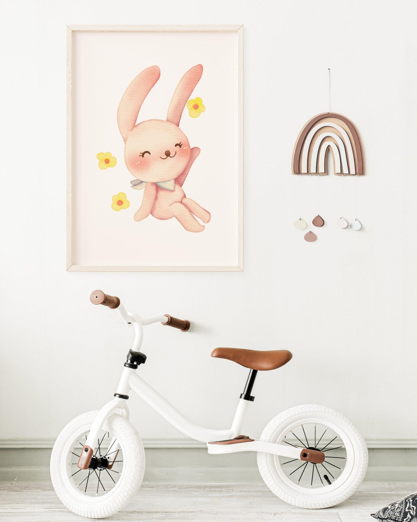 Poster con coniglietto rosa e fiorellini appeso alla parete di una cameretta, con bicicletta bianca e decorazioni arcobaleno.