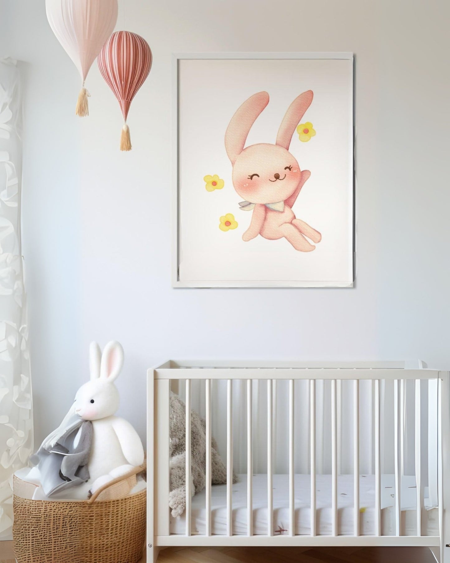 Poster con coniglietto rosa e fiorellini appeso sopra la culla in cameretta, con mongolfiere decorative e pupazzo coniglio su cesta in vimini.