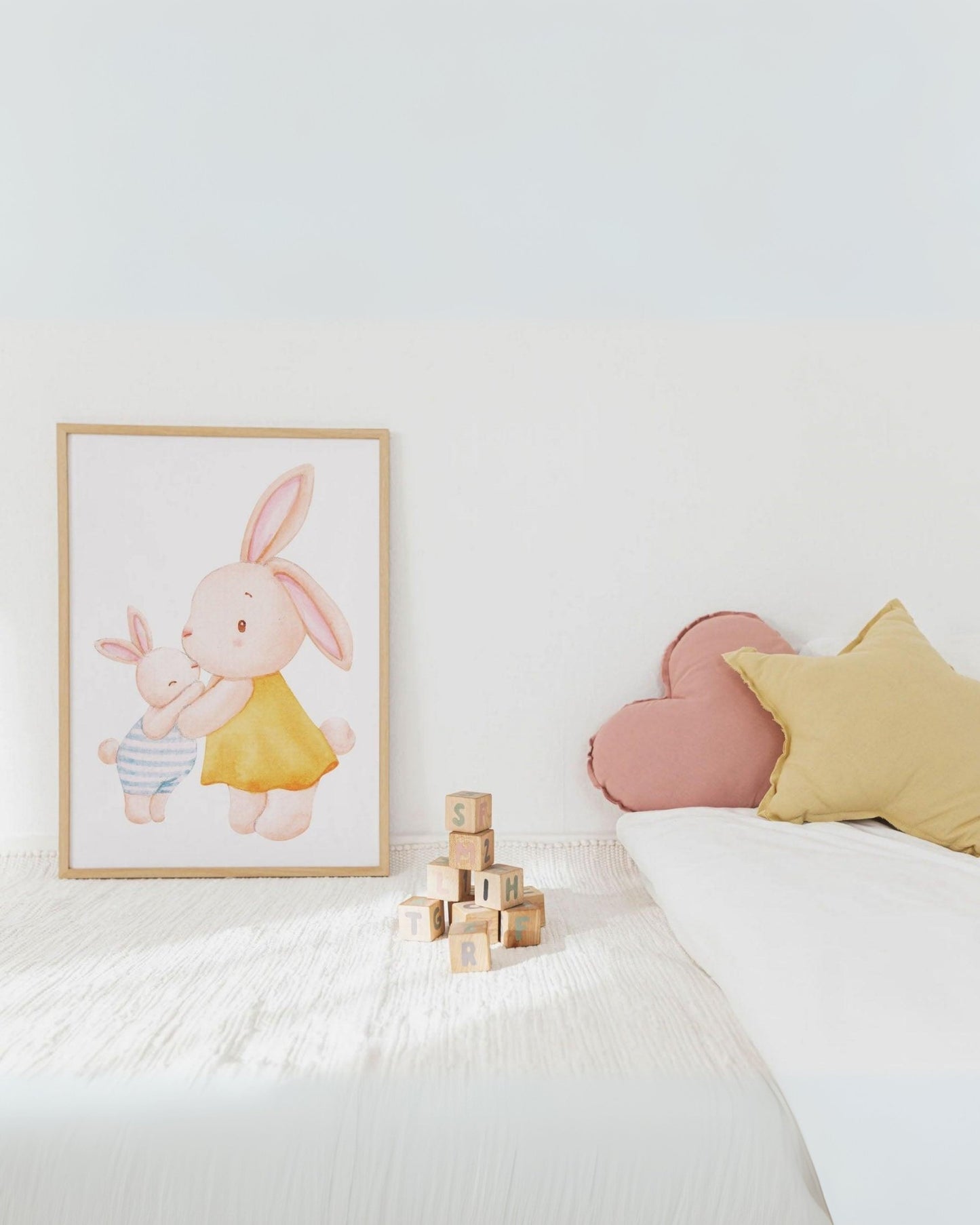 Poster con mamma coniglietta e cucciolo appoggiato su letto per bambini, con cuscini colorati e giochi in legno decorativi.