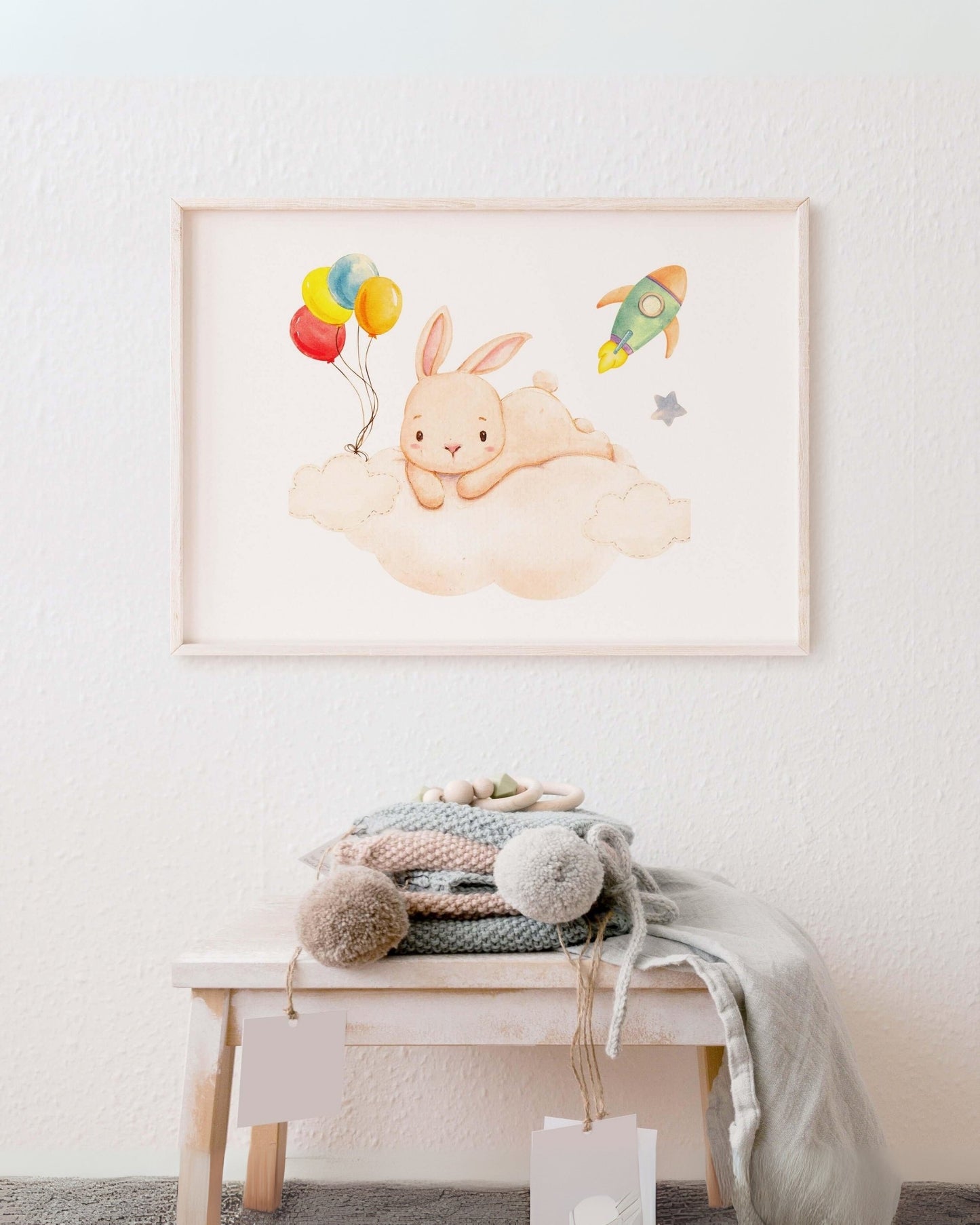 Poster con coniglietto sulla nuvola con palloncini colorati e navicella spaziale appeso alla parete, sopra panchetto con coperte e decorazioni.