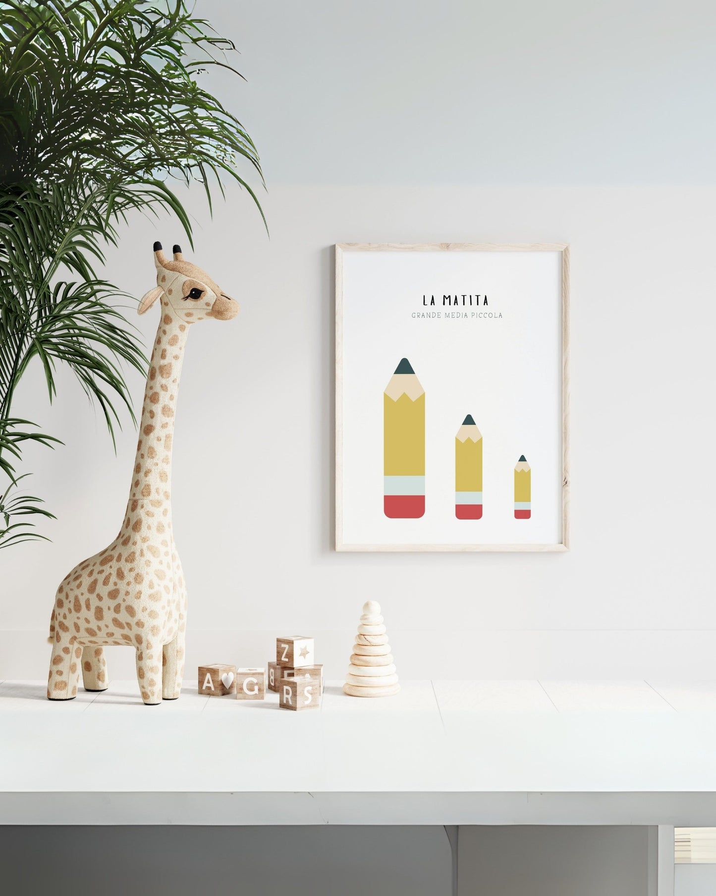 Poster per bambini con tre matite di diverse dimensioni (grande, media, piccola) esposto in cameretta con giraffa di peluche e blocchi di legno decorativi.