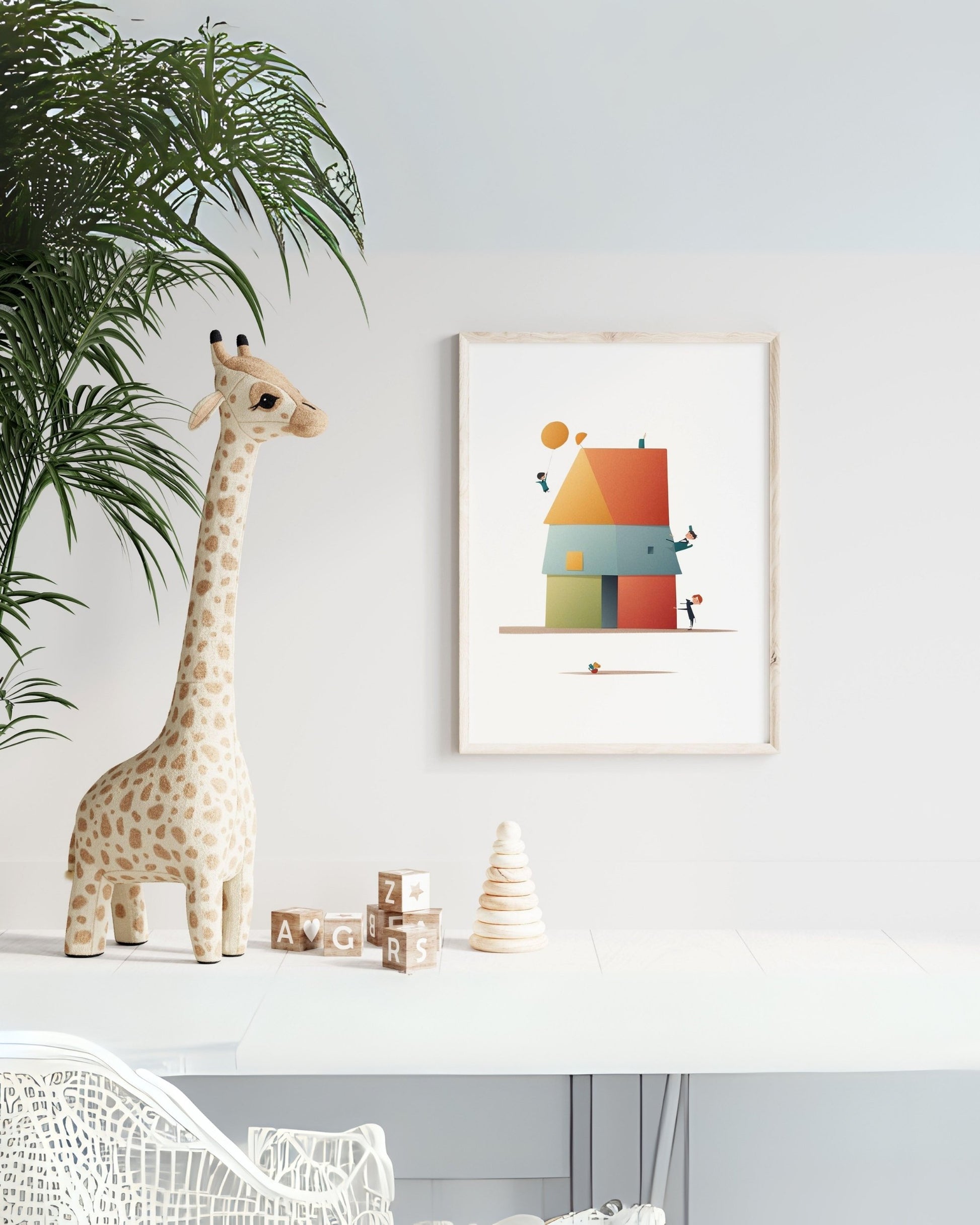 Poster “Casa in Quadro” con casetta stilizzata composta da quadrati e triangoli colorati, appeso a parete bianca accanto a peluche giraffa e giochi per bambini.